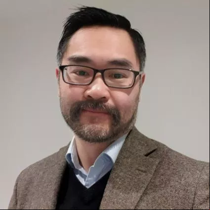 Ed Sum, smiling with glasses and a tweed jack, shirt and jumper